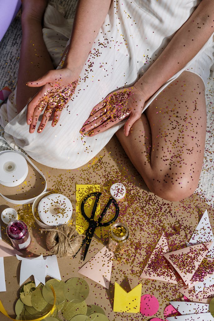 Hands covered in glitter amid crafting materials like paper and scissors, creating a festive mood.